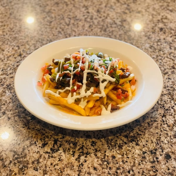 Loaded fries topped with cheese, diced tomatoes, green peppers, black olives, and a white sauce drizzle.