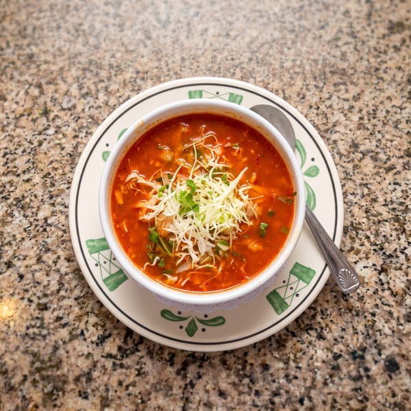 A bowl of red soup with shredded cabbage and cilantro, on a decorative plate with a spoon.