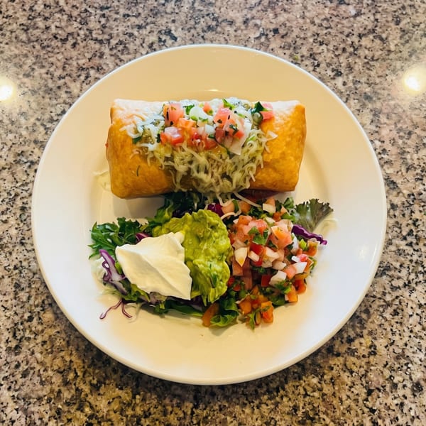 Golden-brown chimichanga topped with cheese, salsa, and cilantro, served with guacamole, sour cream, and salad.