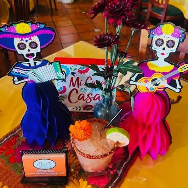 A festive table setting with colorful Day of the Dead figures, flowers, and a margarita.
